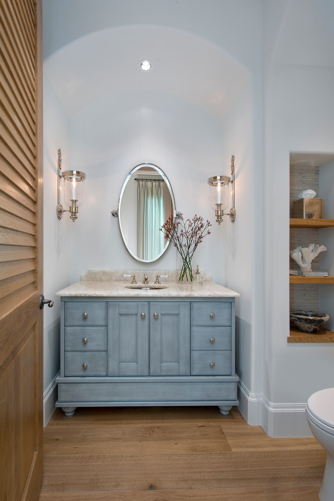 This is an example of a mid-sized beach style powder room in Other with furniture-like cabinets, blue cabinets, white walls, an undermount sink, beige benchtops, a two-piece toilet, medium hardwood floors and brown floor.