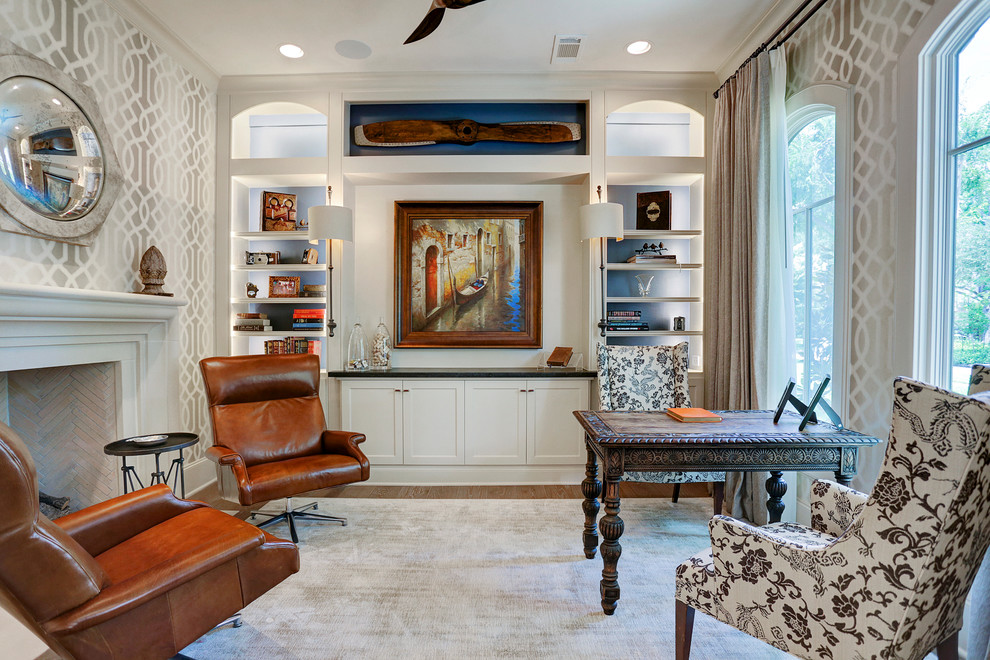 Inspiration for a mid-sized traditional home office in Houston with beige walls, light hardwood floors, a standard fireplace, a stone fireplace surround, a freestanding desk and brown floor.