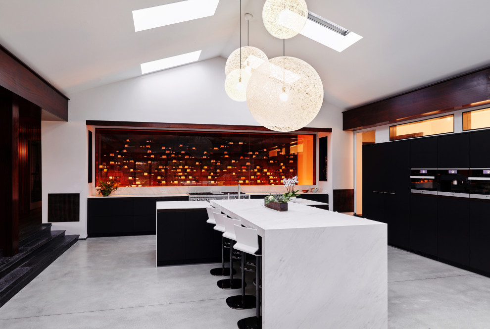 Inspiration for an expansive contemporary kitchen in Philadelphia with an undermount sink, flat-panel cabinets, black cabinets, marble benchtops, black appliances, concrete floors, multiple islands, grey floor, white benchtop and vaulted.