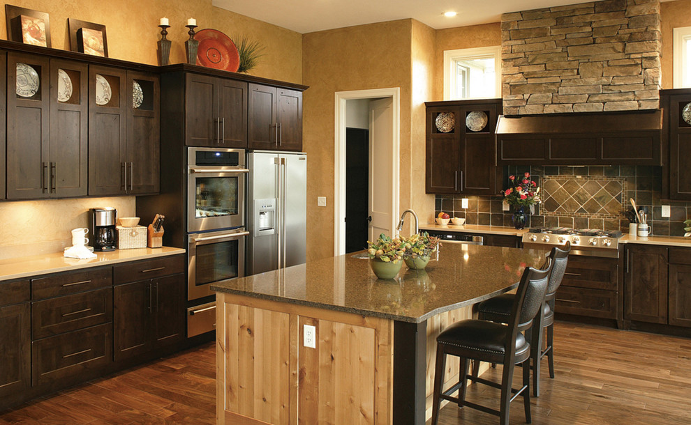 Inspiration for a mid-sized rustic l-shaped medium tone wood floor and brown floor enclosed kitchen remodel in Chicago with an undermount sink, recessed-panel cabinets, dark wood cabinets, quartz countertops, gray backsplash, stone tile backsplash, stainless steel appliances and an island