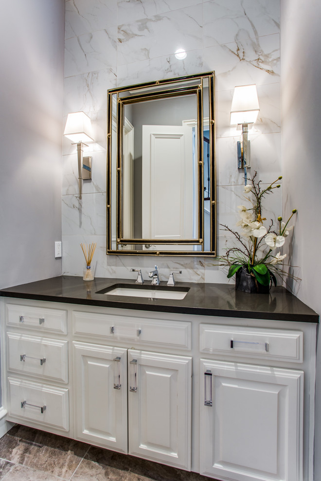 This is an example of a transitional bathroom in Dallas with raised-panel cabinets, white cabinets, beige tile, white tile, grey walls, an undermount sink, beige floor and black benchtops.
