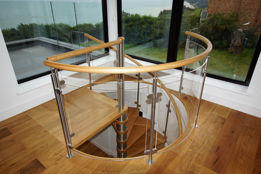 Ejemplo de escalera de caracol moderna de tamaño medio con escalones de madera, contrahuellas de vidrio y barandilla de vidrio