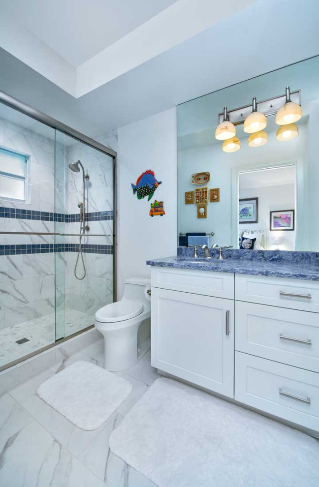 Mid-sized beach style kids bathroom in Miami with shaker cabinets, white cabinets, a drop-in tub, an alcove shower, a two-piece toilet, white tile, ceramic tile, white walls, ceramic floors, an undermount sink, engineered quartz benchtops, white floor, a hinged shower door and blue benchtops.