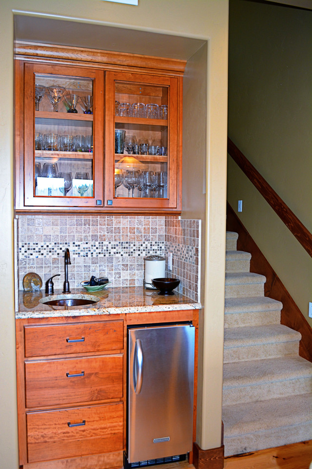 Inspiration for a small arts and crafts single-wall wet bar in Boise with an undermount sink, glass-front cabinets, medium wood cabinets, granite benchtops, beige splashback, ceramic splashback and light hardwood floors.