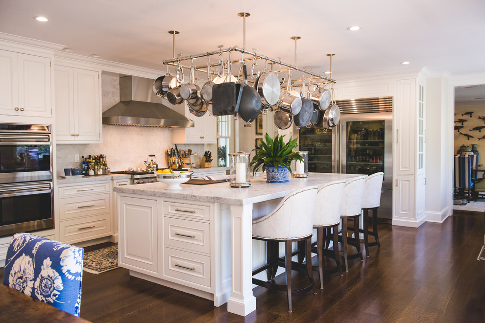 Photo of a traditional l-shaped eat-in kitchen in New York with raised-panel cabinets, white cabinets, white splashback, stainless steel appliances, dark hardwood floors and with island.