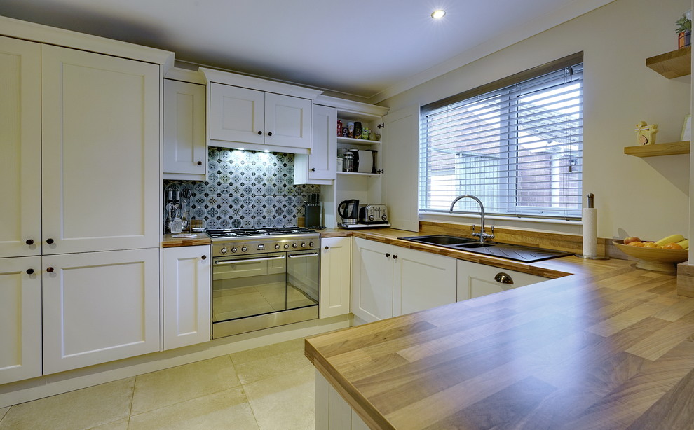This is an example of a mid-sized country u-shaped open plan kitchen in Other with an integrated sink, shaker cabinets, beige cabinets, laminate benchtops, green splashback, ceramic splashback, stainless steel appliances, ceramic floors, a peninsula, beige floor and brown benchtop.