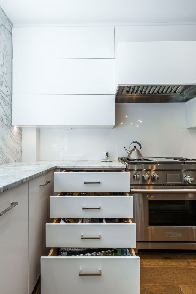 Large minimalist l-shaped medium tone wood floor and brown floor open concept kitchen photo in Montreal with flat-panel cabinets, white cabinets, granite countertops, gray backsplash, granite backsplash, paneled appliances, an island and gray countertops