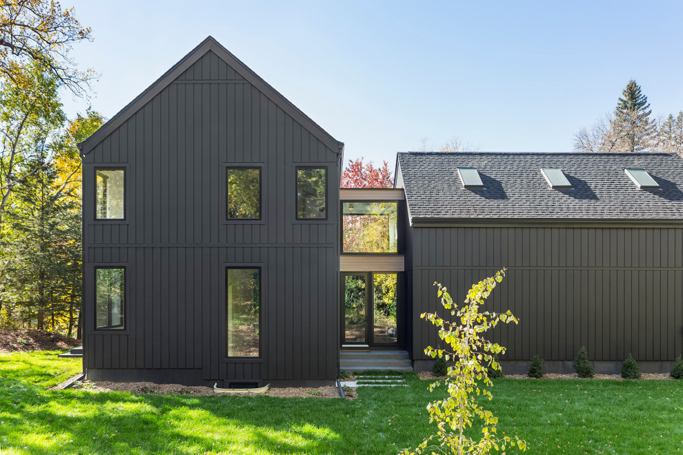 Foto della villa grande nera scandinava a due piani con rivestimento in legno, tetto a capanna, copertura a scandole, tetto nero e pannelli e listelle di legno