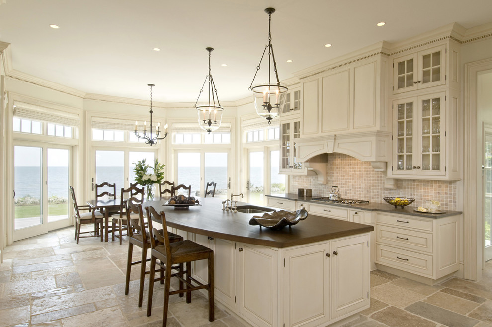 This is an example of a traditional eat-in kitchen in Boston with raised-panel cabinets, white cabinets, limestone splashback and brown benchtop.