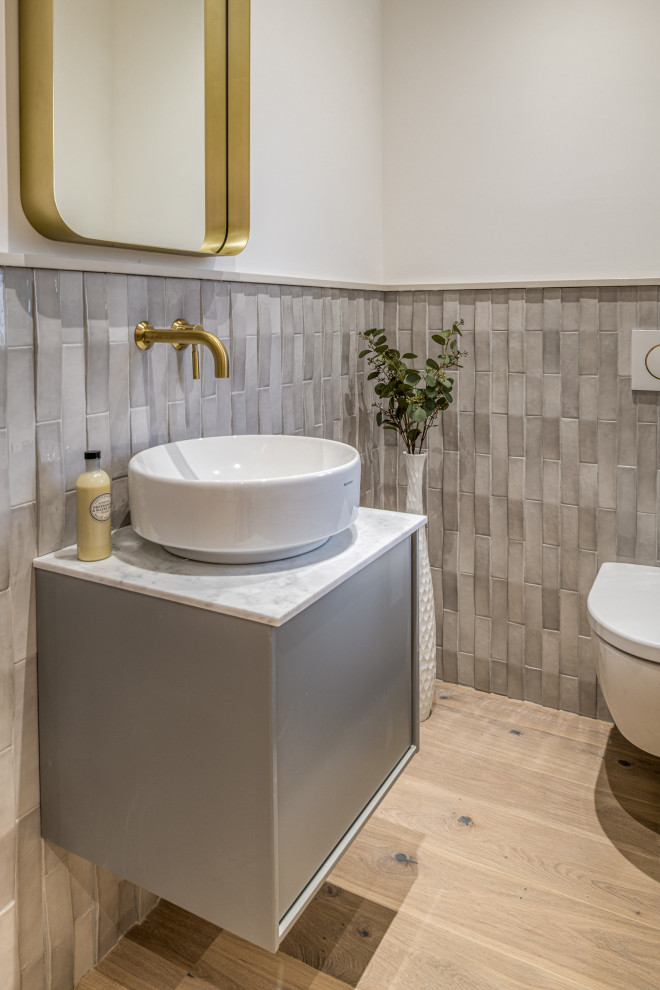 ロンドンにある高級な中くらいなトランジショナルスタイルのおしゃれなトイレ・洗面所 (フラットパネル扉のキャビネット、グレーのキャビネット、壁掛け式トイレ、白いタイル、セラミックタイル、黄色い壁、淡色無垢フローリング、珪岩の洗面台、ベージュの床、グレーの洗面カウンター、アクセントウォール、フローティング洗面台) の写真