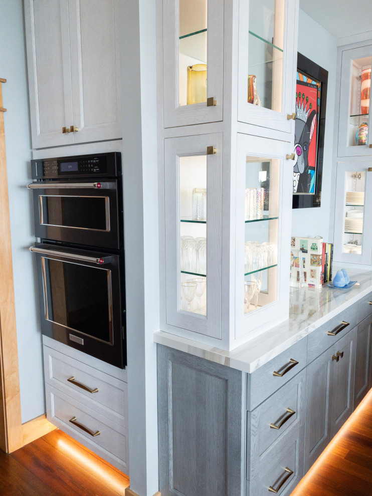Foto på ett stort funkis vit kök, med en undermonterad diskho, släta luckor, grå skåp, bänkskiva i kvarts, vitt stänkskydd, rostfria vitvaror, mellanmörkt trägolv och en köksö