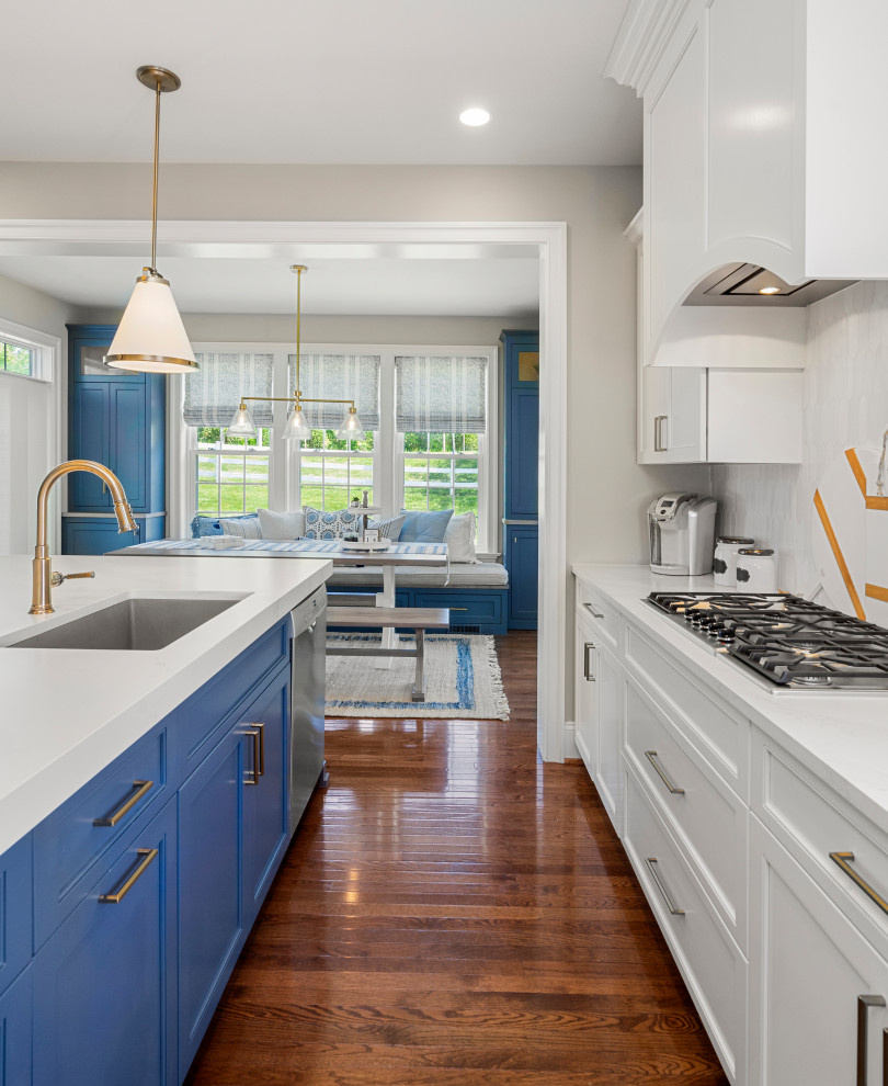 Große Landhausstil Küche mit profilierten Schrankfronten, blauen Schränken, Quarzwerkstein-Arbeitsplatte, Küchenrückwand in Weiß, Küchengeräten aus Edelstahl, dunklem Holzboden, Kücheninsel, braunem Boden und weißer Arbeitsplatte in Sonstige