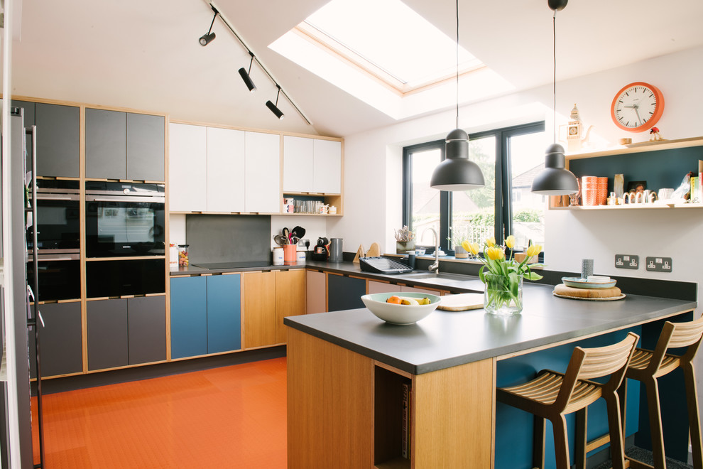 This is an example of a mid-sized contemporary kitchen in Other with flat-panel cabinets, grey splashback, a peninsula, orange floor, grey benchtop, an undermount sink, blue cabinets and black appliances.