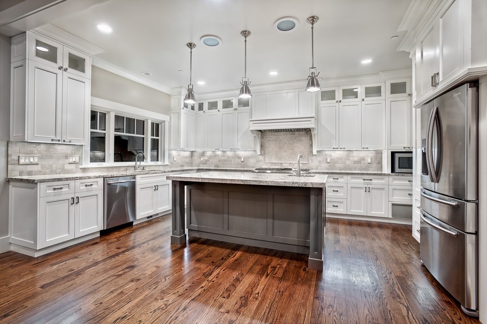 This is an example of a large transitional u-shaped kitchen in Cleveland with an undermount sink, shaker cabinets, white cabinets, granite benchtops, grey splashback, marble splashback, stainless steel appliances, medium hardwood floors, with island and brown floor.