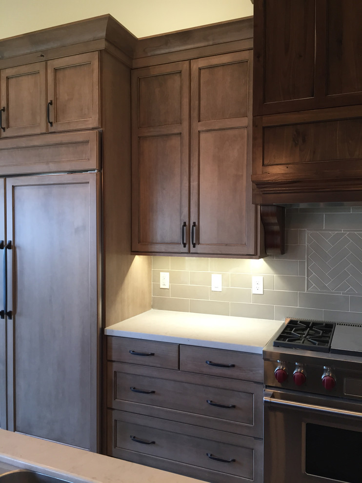 Design ideas for a mid-sized arts and crafts galley eat-in kitchen in Salt Lake City with shaker cabinets, brown cabinets, solid surface benchtops, beige splashback, ceramic splashback, stainless steel appliances, medium hardwood floors and with island.
