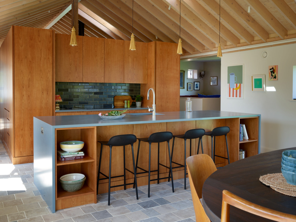 Inspiration for a country kitchen in Other with an integrated sink, flat-panel cabinets, medium wood cabinets, solid surface benchtops, green splashback, ceramic splashback, panelled appliances, limestone floors, with island and blue benchtop.
