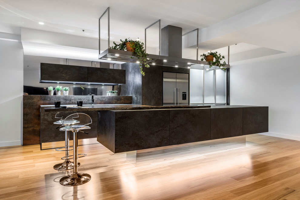 Photo of a mid-sized contemporary galley kitchen in Brisbane with flat-panel cabinets, wood benchtops, metallic splashback, mirror splashback, stainless steel appliances, light hardwood floors and with island.