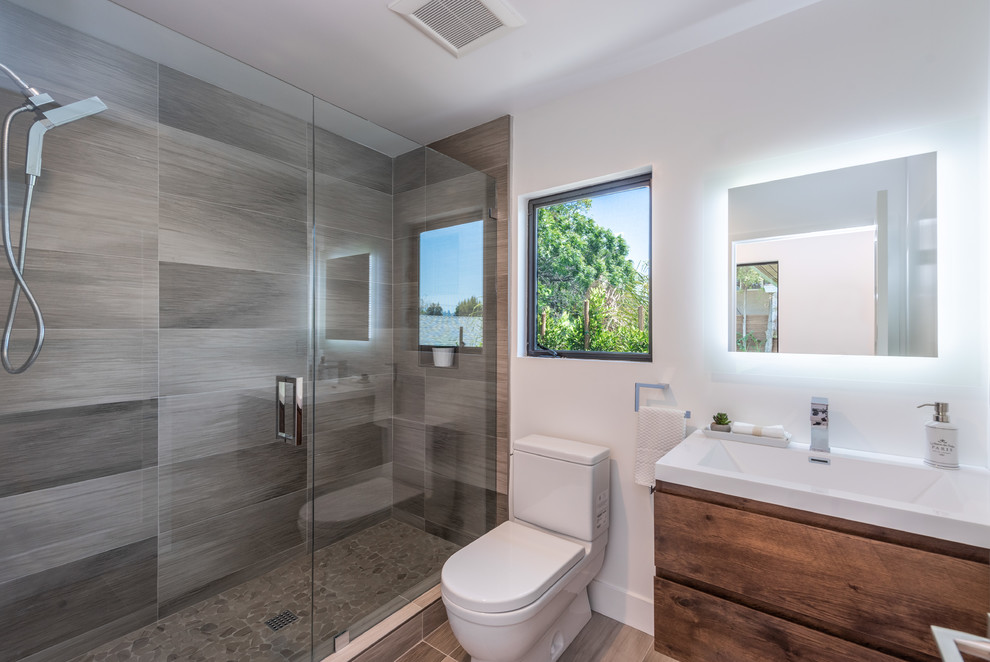 Mid-sized contemporary 3/4 bathroom in Los Angeles with flat-panel cabinets, medium wood cabinets, brown tile, white walls, a console sink, brown floor, a hinged shower door, a two-piece toilet, porcelain tile, porcelain floors, engineered quartz benchtops and white benchtops.