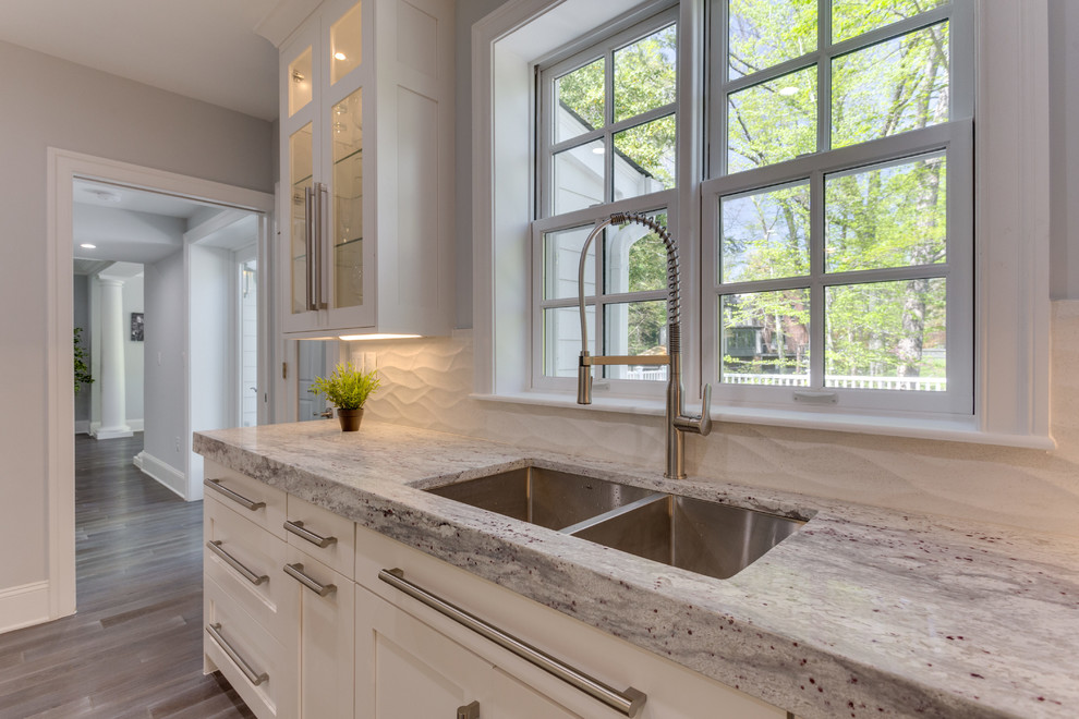 Inspiration for a large transitional l-shaped medium tone wood floor open concept kitchen remodel in DC Metro with a double-bowl sink, shaker cabinets, white cabinets, marble countertops, white backsplash, porcelain backsplash, stainless steel appliances and an island