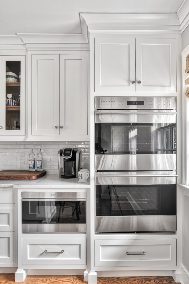 Example of a large transitional l-shaped light wood floor and beige floor eat-in kitchen design in New York with an undermount sink, beaded inset cabinets, white cabinets, marble countertops, white backsplash, subway tile backsplash, stainless steel appliances, an island and gray countertops