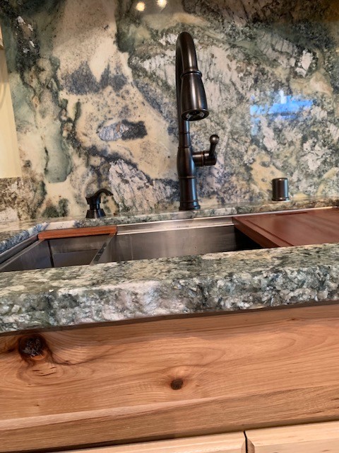 Open concept kitchen - mid-sized rustic medium tone wood floor and brown floor open concept kitchen idea with an undermount sink, flat-panel cabinets, light wood cabinets, granite countertops, gray backsplash, stone slab backsplash, stainless steel appliances and gray countertops