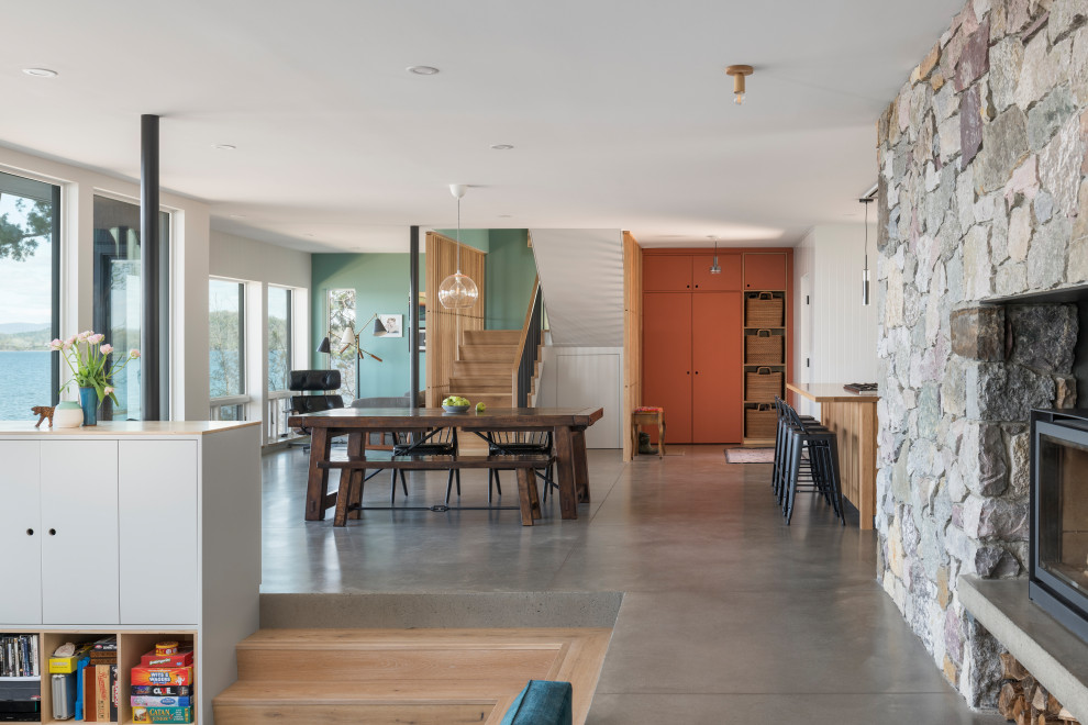 Cette image montre une salle à manger ouverte sur le salon minimaliste de taille moyenne avec un mur vert, sol en béton ciré, un poêle à bois, un manteau de cheminée en pierre et un sol gris.