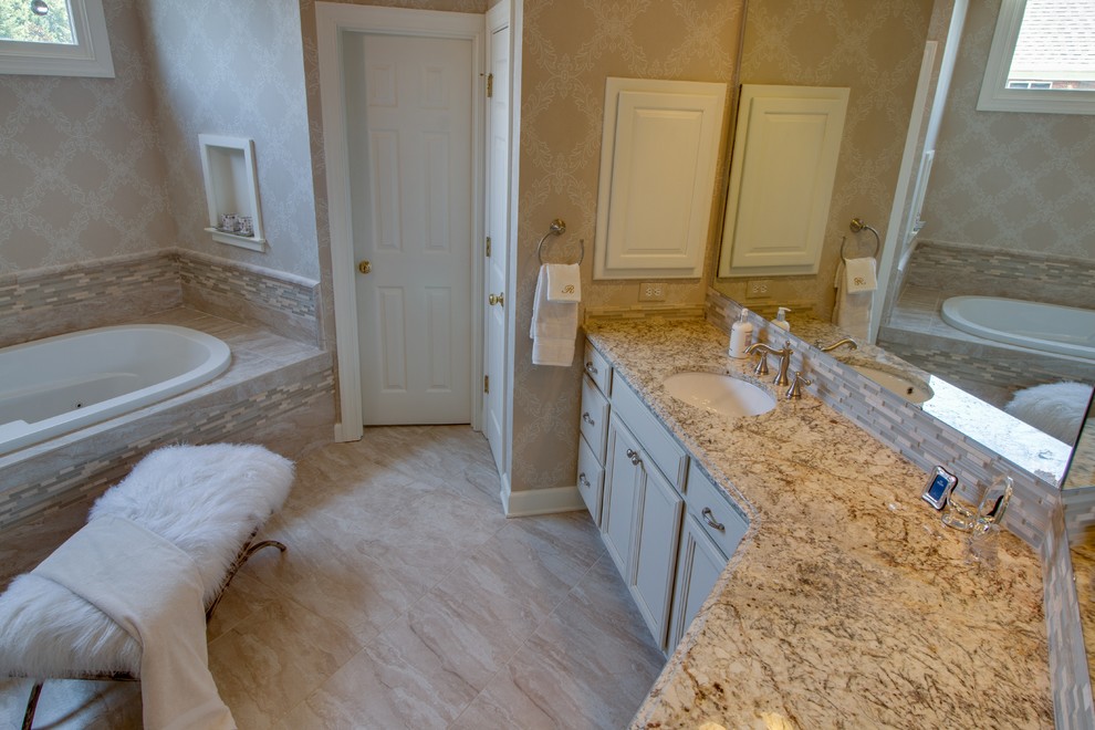 Large contemporary master bathroom in Charlotte with recessed-panel cabinets, beige cabinets, a drop-in tub, an alcove shower, beige tile, limestone, beige walls, limestone floors, an undermount sink, laminate benchtops, beige floor and a hinged shower door.