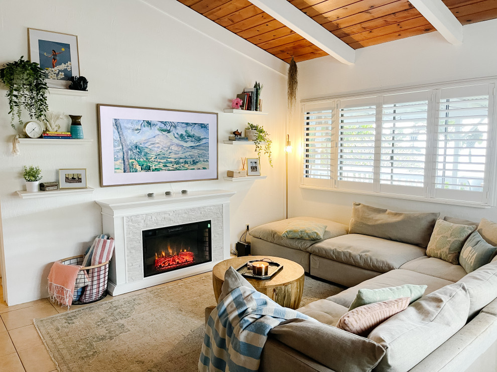 This is an example of a medium sized world-inspired living room in Hawaii with white walls, porcelain flooring, a standard fireplace, a wall mounted tv, beige floors and exposed beams.