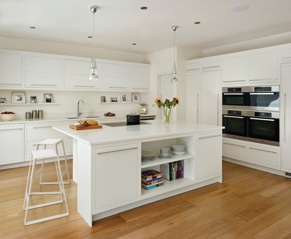 Design ideas for a large scandinavian l-shaped kitchen in London with an undermount sink, flat-panel cabinets, white cabinets, white splashback, panelled appliances, medium hardwood floors and with island.