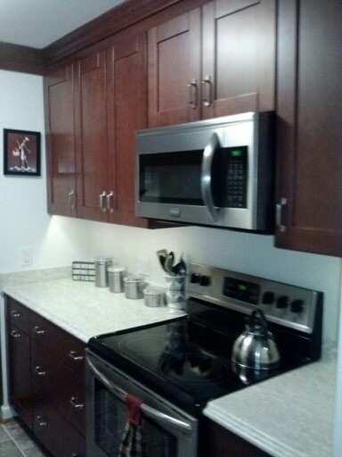 Small transitional l-shaped vinyl floor enclosed kitchen photo in Richmond with a drop-in sink, shaker cabinets, dark wood cabinets, granite countertops, white backsplash and stainless steel appliances