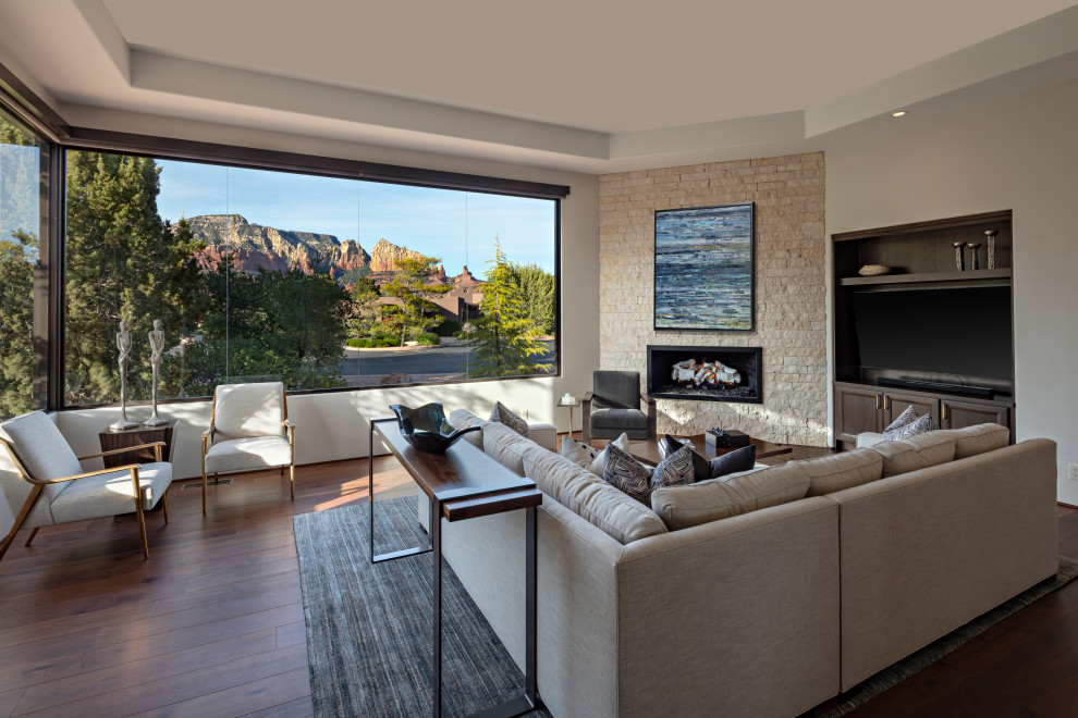 This is an example of a modern enclosed living room in Phoenix with white walls, medium hardwood flooring, a corner fireplace, a stone fireplace surround, a built-in media unit and brown floors.