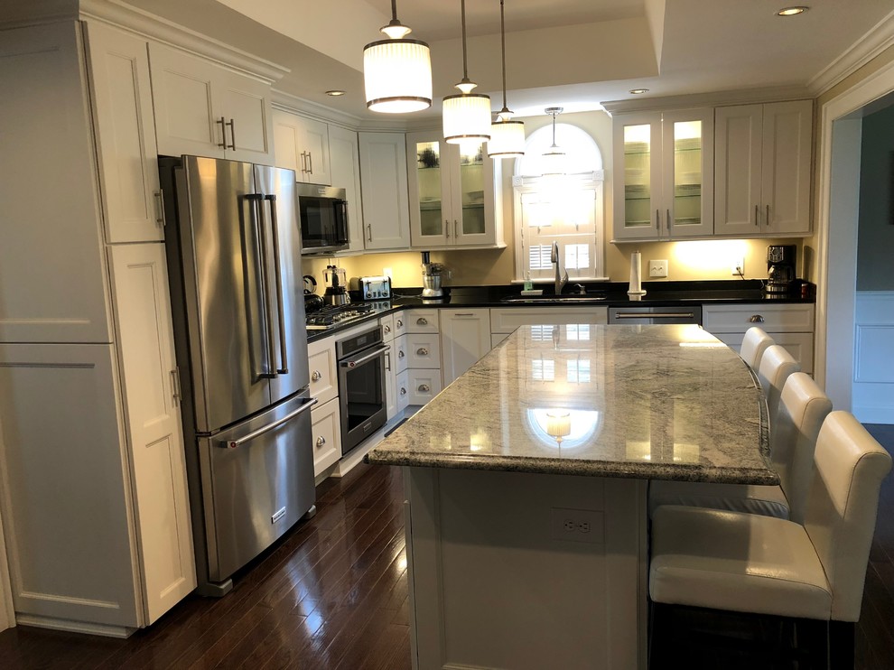 Eat-in kitchen - large transitional l-shaped medium tone wood floor and brown floor eat-in kitchen idea in New York with a double-bowl sink, shaker cabinets, white cabinets, quartzite countertops, beige backsplash, stainless steel appliances, an island and black countertops