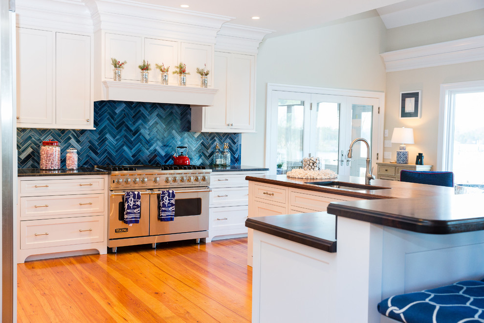 Inspiration for a beach style eat-in kitchen in Baltimore with limestone benchtops, blue splashback, stainless steel appliances, light hardwood floors and a peninsula.