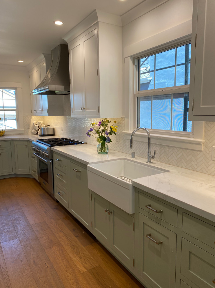 This is an example of a transitional galley kitchen in San Francisco with a farmhouse sink, shaker cabinets, green cabinets, quartz benchtops, white splashback, mosaic tile splashback, stainless steel appliances, light hardwood floors, no island, beige floor and white benchtop.