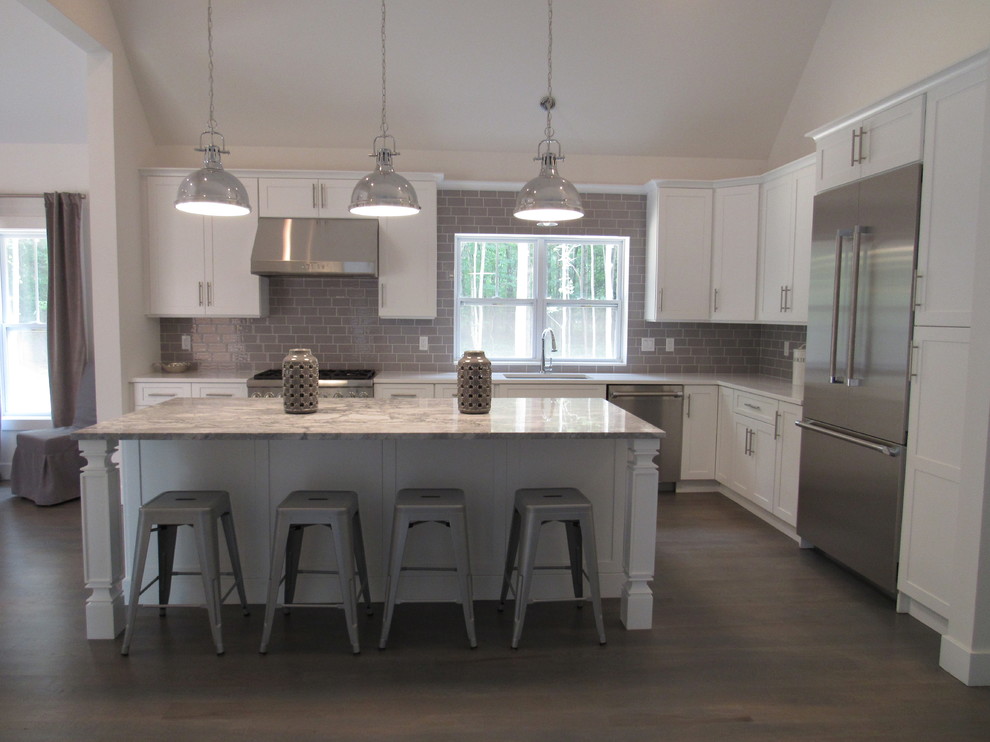 This is an example of a mid-sized transitional l-shaped open plan kitchen in New York with an undermount sink, shaker cabinets, white cabinets, marble benchtops, grey splashback, subway tile splashback, stainless steel appliances, dark hardwood floors, with island and brown floor.