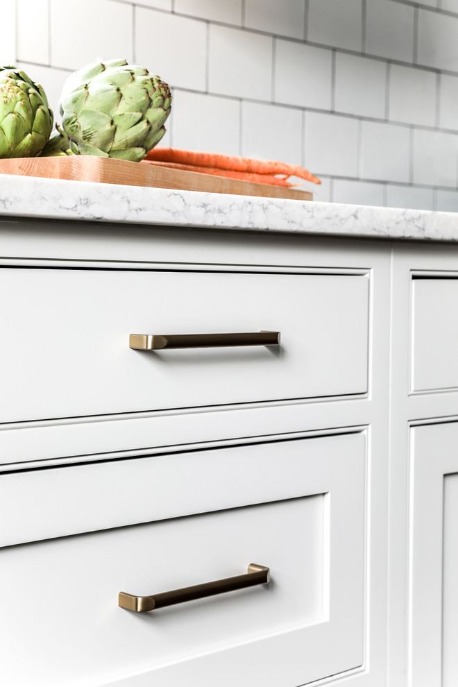 Example of a transitional l-shaped medium tone wood floor and brown floor eat-in kitchen design in Boston with a farmhouse sink, beaded inset cabinets, white cabinets, quartz countertops, white backsplash, subway tile backsplash, stainless steel appliances, an island and gray countertops