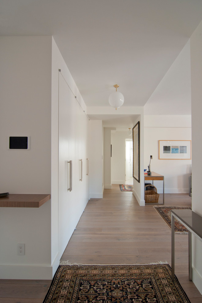 This is an example of a mid-sized contemporary hallway in New York with white walls, medium hardwood floors and brown floor.