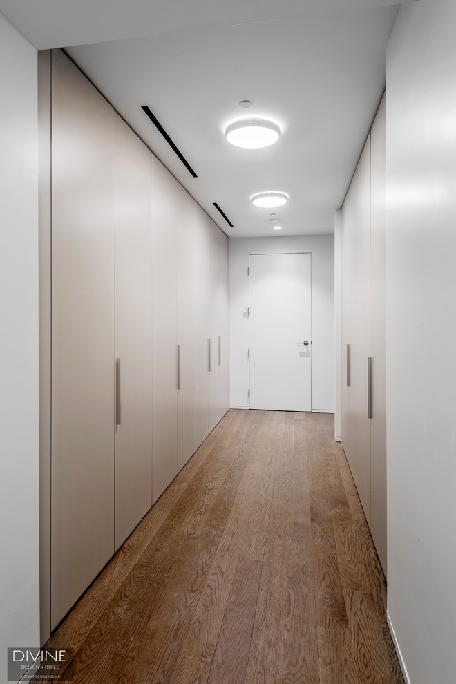 This is an example of a large contemporary gender-neutral built-in wardrobe in Boston with flat-panel cabinets, beige cabinets, medium hardwood floors and brown floor.