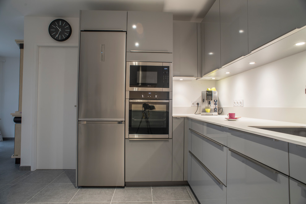 Design ideas for a mid-sized modern u-shaped open plan kitchen in Bordeaux with an integrated sink, flat-panel cabinets, grey cabinets, solid surface benchtops, white splashback, stainless steel appliances, ceramic floors, no island and grey floor.