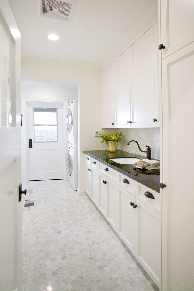 Photo of a contemporary galley laundry room in Los Angeles with recessed-panel cabinets, white cabinets, granite benchtops, white walls and a stacked washer and dryer.