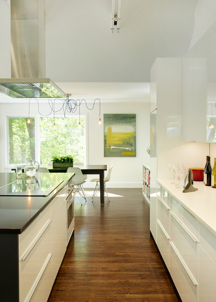 Photo of a mid-sized contemporary galley eat-in kitchen in New York with a single-bowl sink, flat-panel cabinets, white cabinets, quartz benchtops, white splashback, stainless steel appliances, dark hardwood floors and with island.