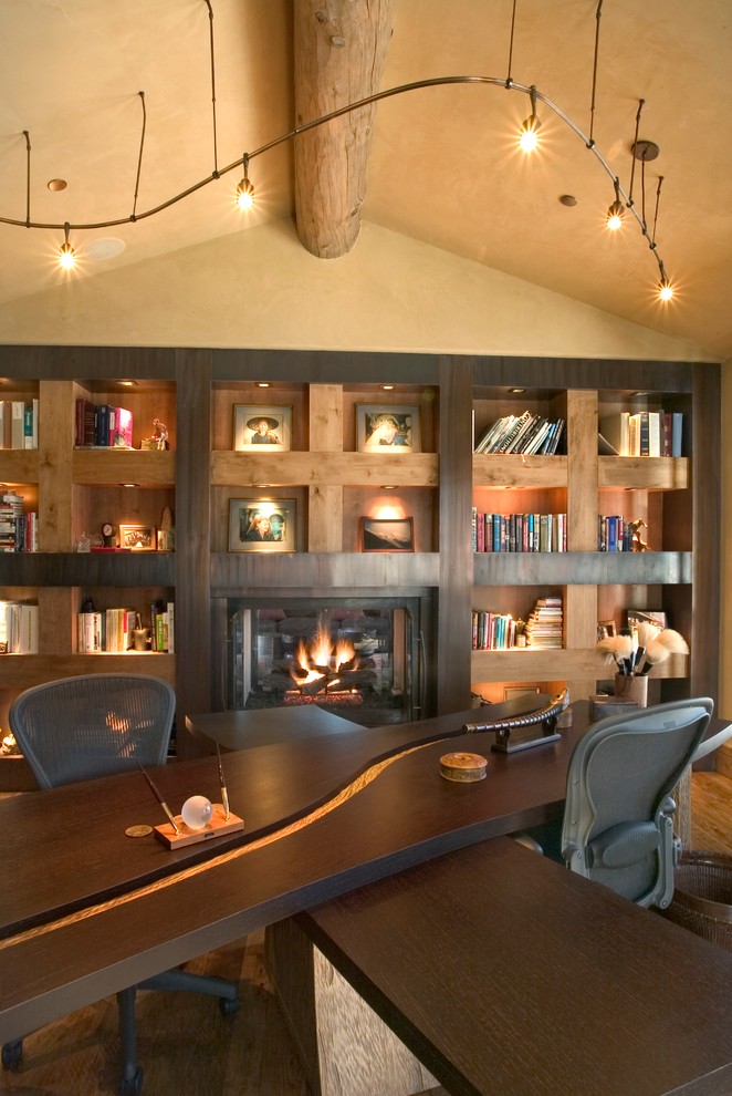 Large modern home office in Denver with beige walls, medium hardwood floors, a standard fireplace, a metal fireplace surround, a freestanding desk, a library, brown floor and vaulted.
