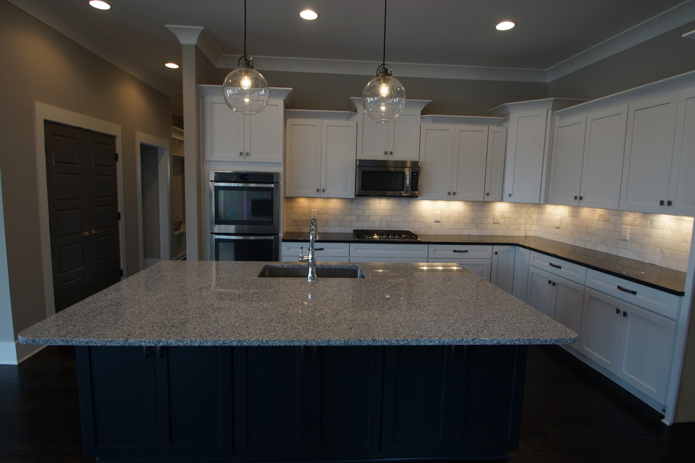 Large transitional dark wood floor kitchen photo in Nashville with an undermount sink, shaker cabinets, white cabinets, granite countertops, white backsplash, stainless steel appliances and an island