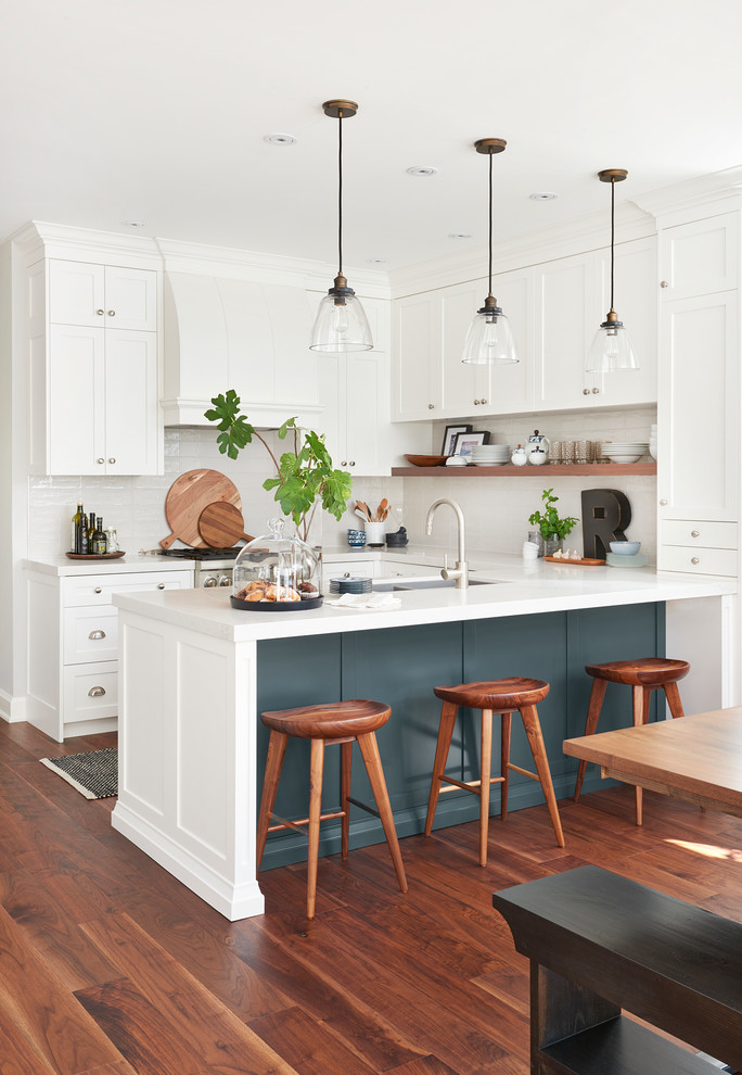 Inspiration for a transitional u-shaped open plan kitchen in Toronto with an undermount sink, shaker cabinets, white cabinets, white splashback, subway tile splashback, stainless steel appliances, medium hardwood floors, a peninsula and brown floor.