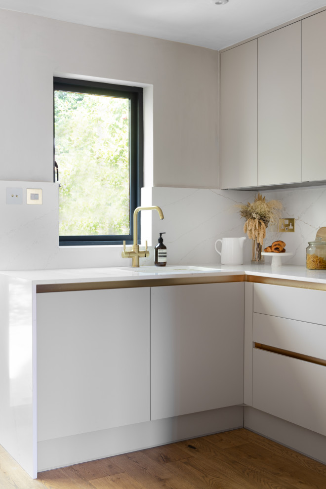 Photo of a small contemporary u-shaped open plan kitchen in Manchester with an integrated sink, flat-panel cabinets, beige cabinets, solid surface benchtops, white splashback, black appliances, light hardwood floors, no island and yellow benchtop.