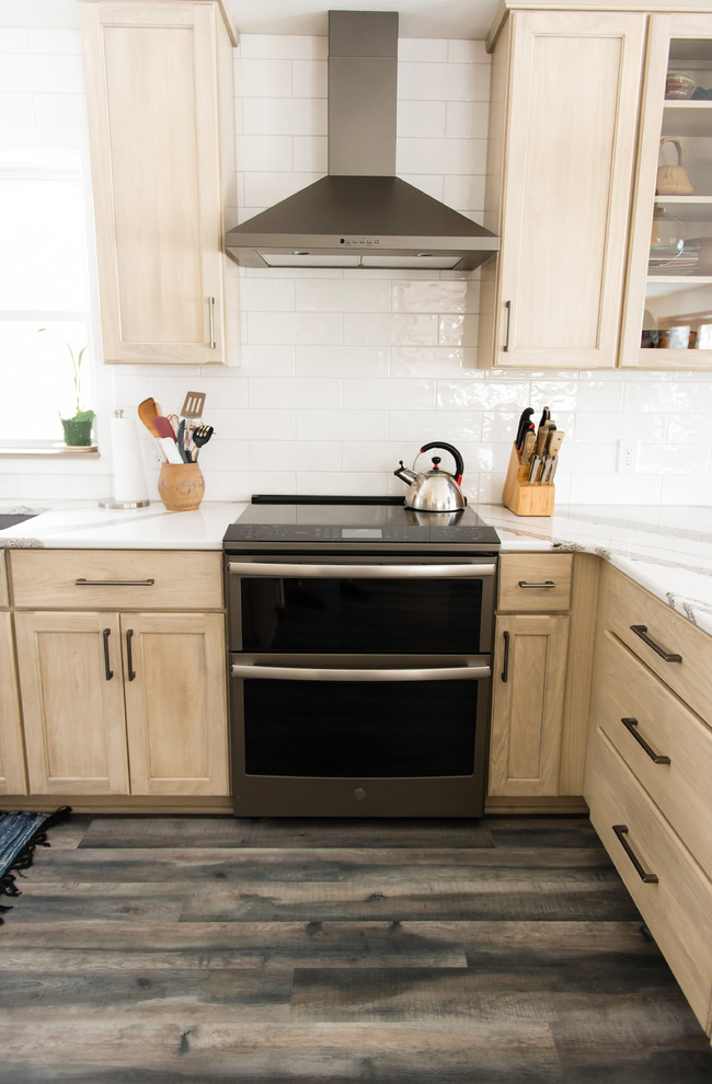 Mid-sized transitional u-shaped vinyl floor and brown floor enclosed kitchen photo with an undermount sink, flat-panel cabinets, beige cabinets, quartz countertops, white backsplash, subway tile backsplash, black appliances, a peninsula and white countertops