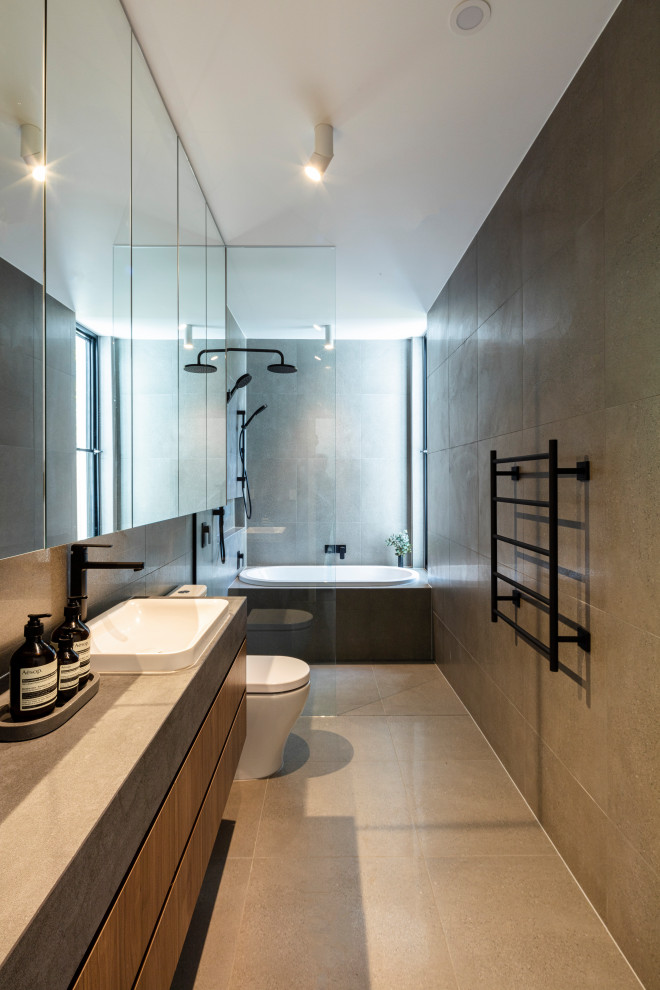Photo of a small contemporary kids bathroom in Melbourne with flat-panel cabinets, dark wood cabinets, a drop-in tub, an open shower, a one-piece toilet, gray tile, porcelain tile, grey walls, porcelain floors, a drop-in sink, solid surface benchtops, grey floor, an open shower, grey benchtops, a single vanity and a floating vanity.