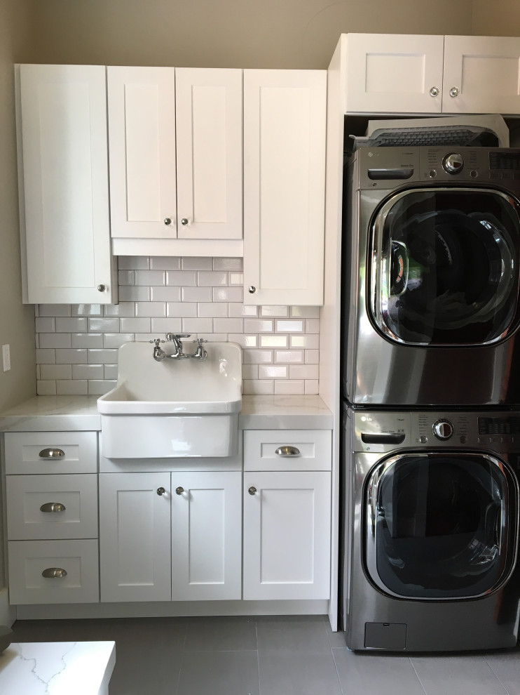 Mid-sized arts and crafts single-wall dedicated laundry room in Orlando with a farmhouse sink, shaker cabinets, white cabinets, quartz benchtops, grey walls, porcelain floors, a stacked washer and dryer, grey floor and white benchtop.