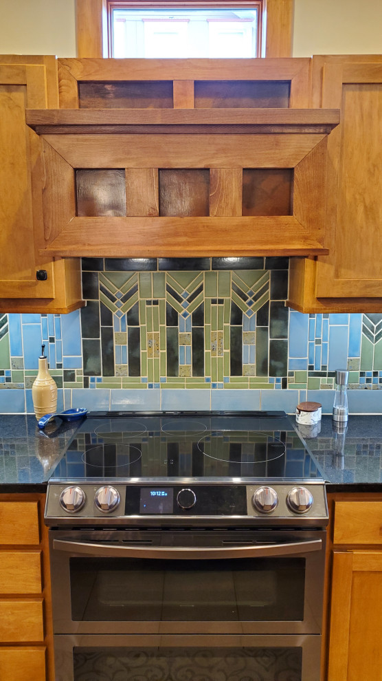 Photo of a large arts and crafts l-shaped eat-in kitchen in Minneapolis with a drop-in sink, shaker cabinets, brown cabinets, blue splashback, terra-cotta splashback, black appliances, with island and black benchtop.