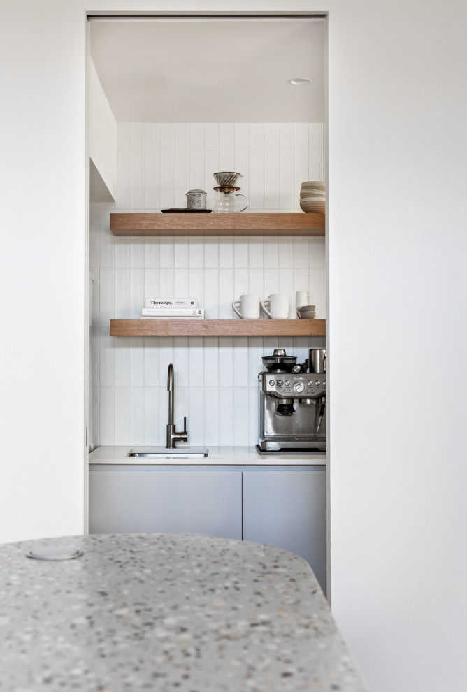 Design ideas for a small contemporary single-wall utility room in Sydney with an undermount sink, grey cabinets, quartz benchtops, white splashback, ceramic splashback, white walls, porcelain floors, a stacked washer and dryer, grey floor and white benchtop.